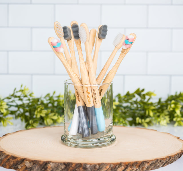 Wellnesse biodegradable toothbrushes in multiple bristle colors grouped together in a glass jar