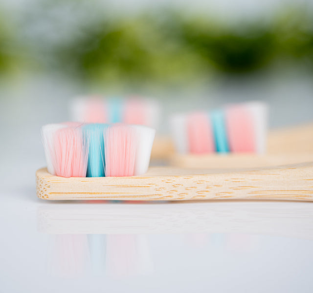 Close-up of Wellnesse dense bristle toothbrush heads in pink, white, and teal colors