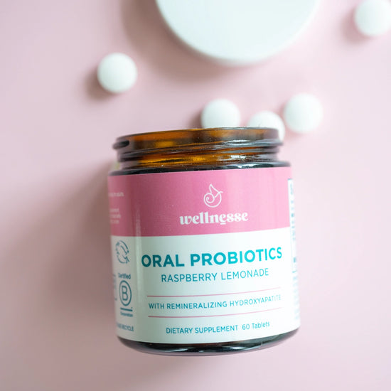 Oral probiotics in raspberry lemonade flavor by Wellnesse, shown in a glass jar with white tablets on a pink background.