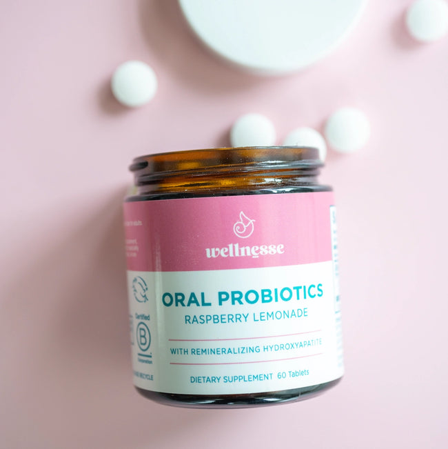 Oral probiotics in raspberry lemonade flavor by Wellnesse, shown in a glass jar with white tablets on a pink background.
