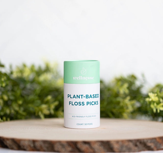 Wellnesse biodegradable floss picks in a mint green container labeled plant-based on a wooden surface