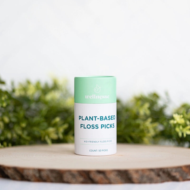 Wellnesse biodegradable floss picks in a mint green container labeled plant-based on a wooden surface