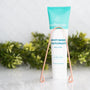 Wellnesse fluoride-free mint whitening toothpaste tube with a copper tongue scraper in front of greenery.