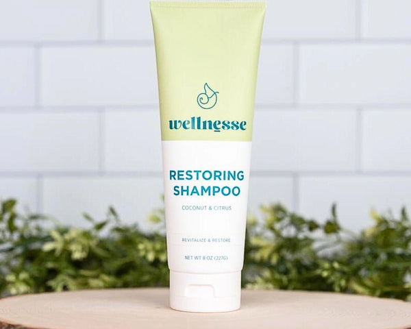 Restoring shampoo by Wellnesse in a coconut and citrus formula, displayed upright on a wood slice with greenery.