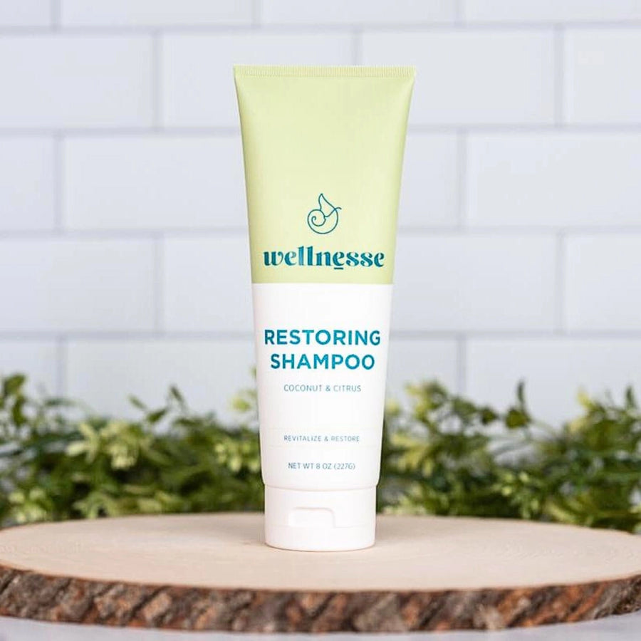 Restoring shampoo by Wellnesse in a coconut and citrus formula, displayed upright on a wood slice with greenery.