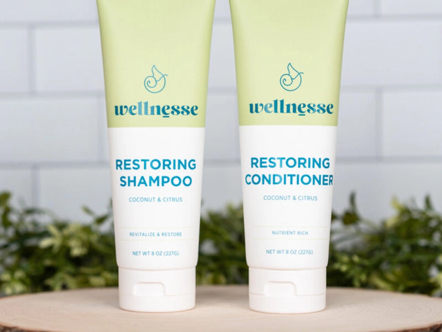 Restoring conditioner with coconut and citrus by Wellnesse, shown next to matching shampoo on a wooden display with greenery.