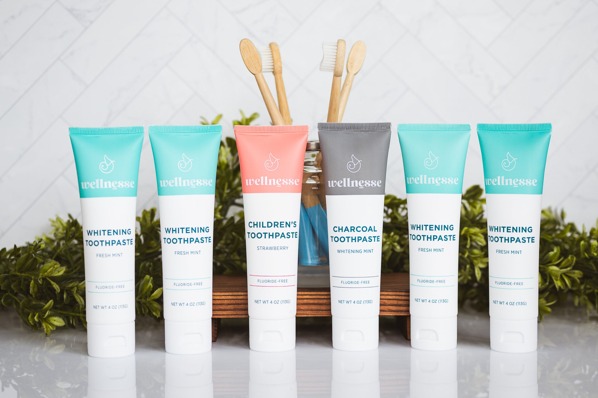 Organic hydroxyapatite toothpaste lineup including whitening mint, charcoal, and children's strawberry flavors with bamboo toothbrushes in a glass jar