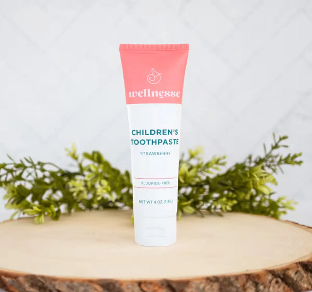 Wellnesse natural toothpaste for kids in strawberry flavor with a pink tube on a wood slice