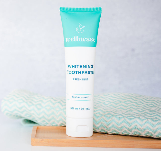 Fluoride-free mint whitening toothpaste tube on a bamboo tray with a teal chevron cloth.