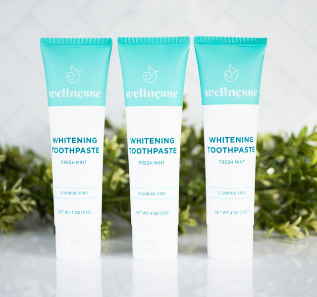 Best all natural whitening toothpaste trio from Wellnesse in fresh mint flavor, fluoride-free formula, displayed with green foliage backdrop.