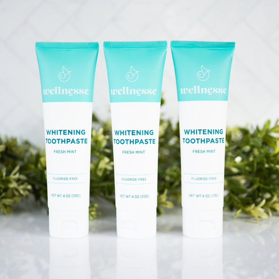 Best all natural whitening toothpaste trio from Wellnesse in fresh mint flavor, fluoride-free formula, displayed with green foliage backdrop.