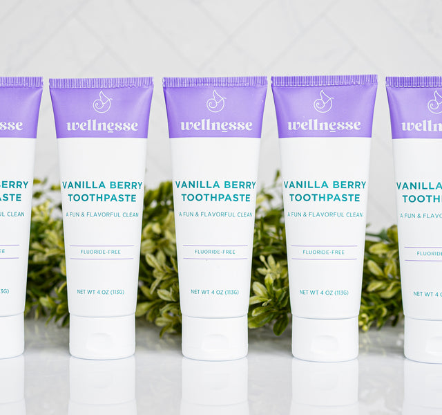 Fluoride-free toothpaste by Wellnesse in Vanilla Berry flavor shown as five identical tubes lined up in a row against a white herringbone tile backdrop.