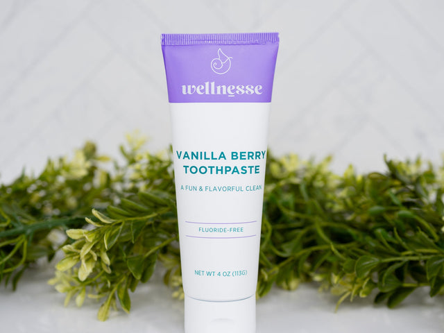 Tube of Wellnesse Vanilla Berry toothpaste on a white surface with greenery in the background
