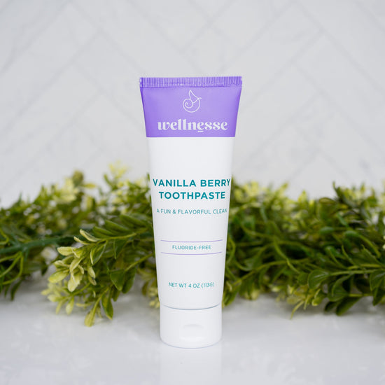 Tube of Wellnesse Vanilla Berry toothpaste on a white surface with greenery in the background