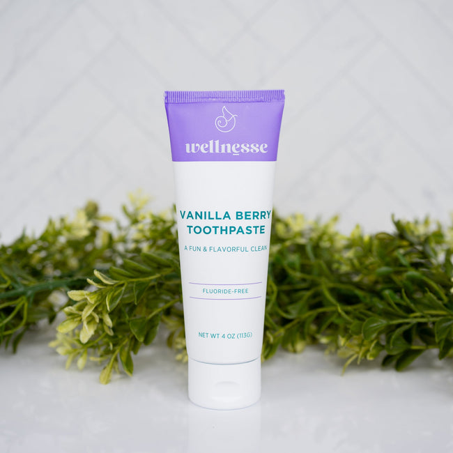Tube of Wellnesse Vanilla Berry toothpaste on a white surface with greenery in the background