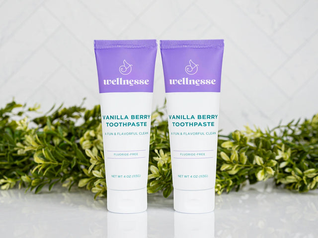 Two tubes of Wellnesse vanilla berry toothpaste with purple caps, fluoride-free for a fun and flavorful clean.