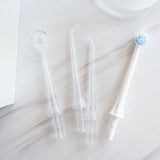 Water flosser heads including three clear tips and one white electric toothbrush head on a light marble surface.
