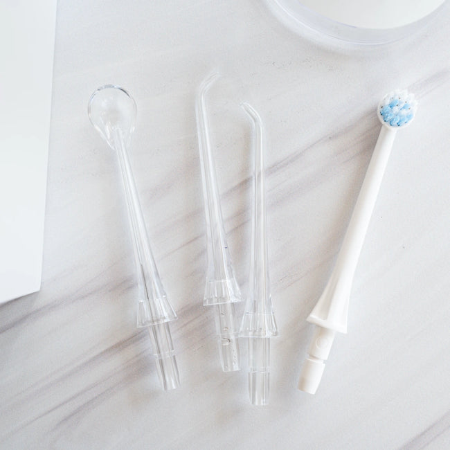Water flosser heads including three clear tips and one white electric toothbrush head on a light marble surface.