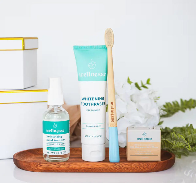 Wellnesse mini gift set with whitening toothpaste, hand sanitizer, bamboo toothbrush, and floss on a tray