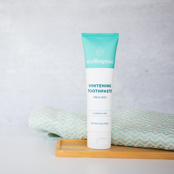 Wellnesse whitening toothpaste standing on a bamboo tray with a folded teal towel from the oral care set