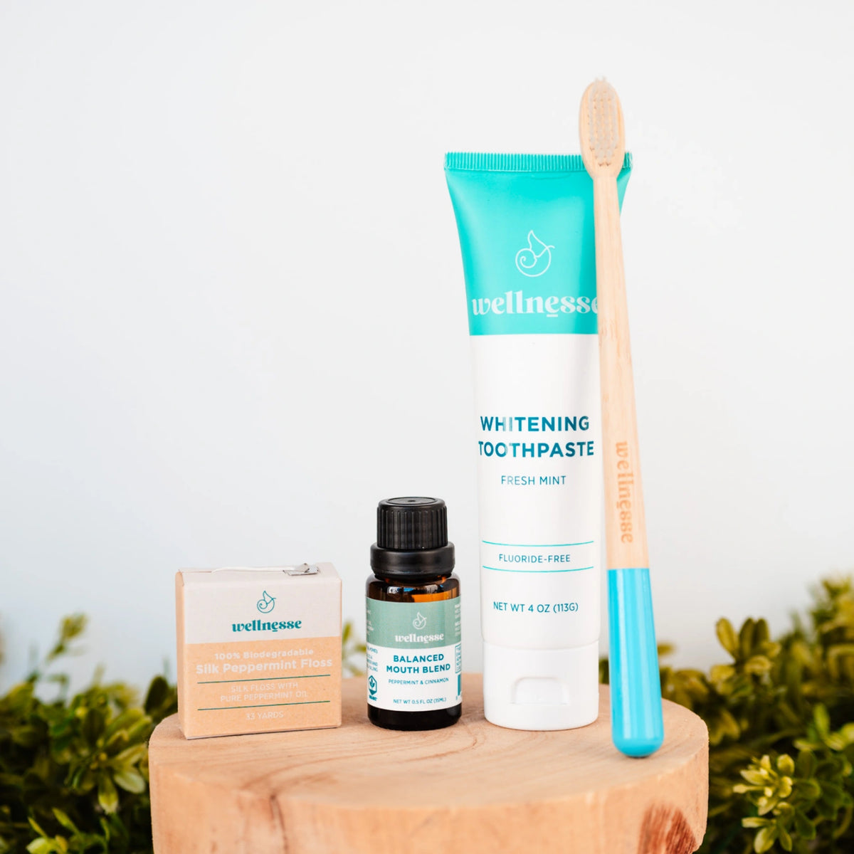 Whitening mint toothpaste by Wellnesse displayed with bamboo toothbrush, floss, and mouth blend on wooden surface.