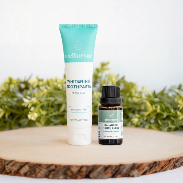 Wellnesse whitening toothpaste in fresh mint paired with Balanced Mouth Blend peppermint and cinnamon oil on a wood slice.