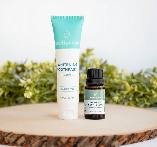 Wellnesse whitening toothpaste in fresh mint paired with Balanced Mouth Blend peppermint and cinnamon oil on a wood slice.