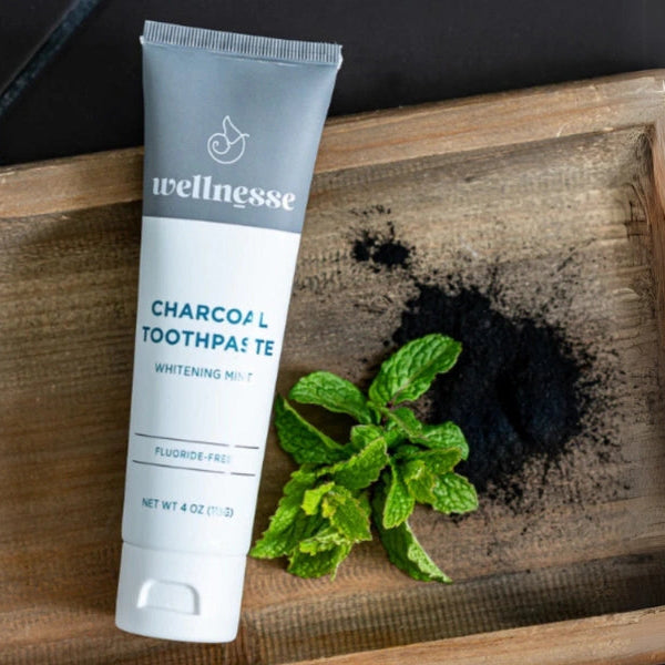 Wellnesse charcoal toothpaste on a rustic wood tray with fresh mint leaves and activated charcoal powder