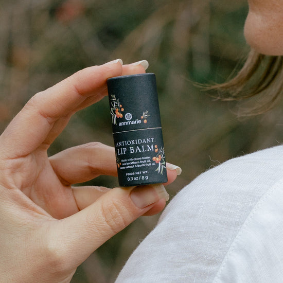 Hand holding the Antioxidant Lip Balm in a natural outdoor setting with soft-focus greenery