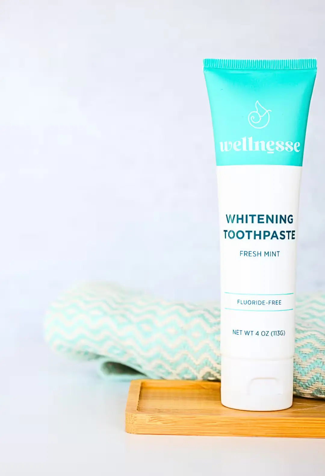 Mint whitening toothpaste in a Wellnesse fluoride-free tube, placed on a wooden tray with a patterned mint towel in the background.